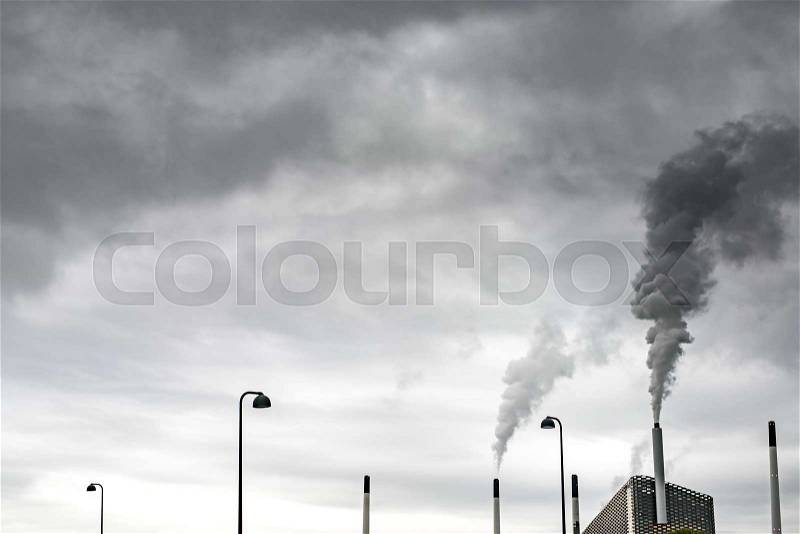 Amager Bakke waste-to-energy plant with steaming chimney on the background of the cloudy gray sky in Copenhagen. There are few chimneys and street lights and next to it. Horizontal, stock photo