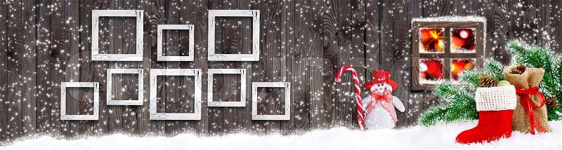 Christmas banner with eight empty photo frames, Snowman with candy cane, Santa boot, bag with gifts and cones on wooden wall background and glowing lights outside the window, stock photo