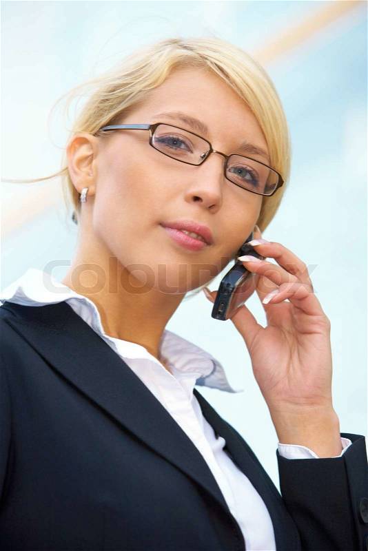 Young businesswoman looking at camera outside office building, using mobile phone, stock photo