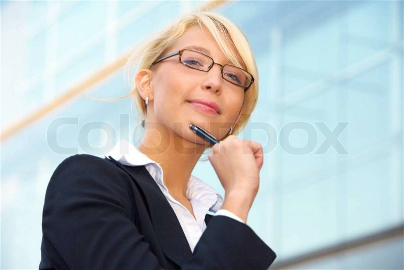 Young businesswoman looking at camera outside office building, holding pen, stock photo
