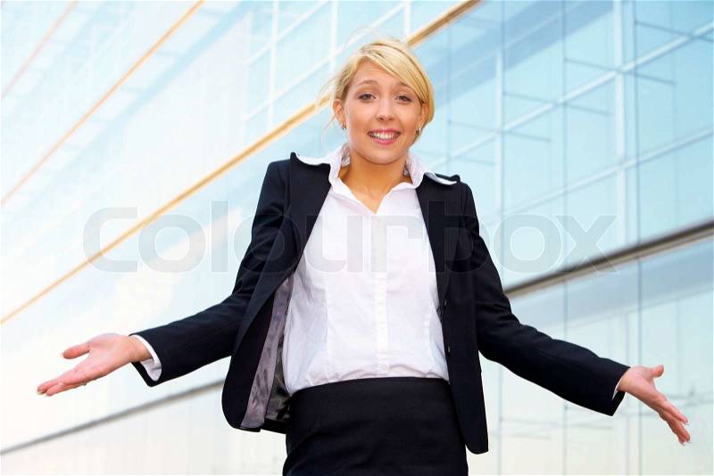 Young businesswoman standing with arms open outside office building, stock photo