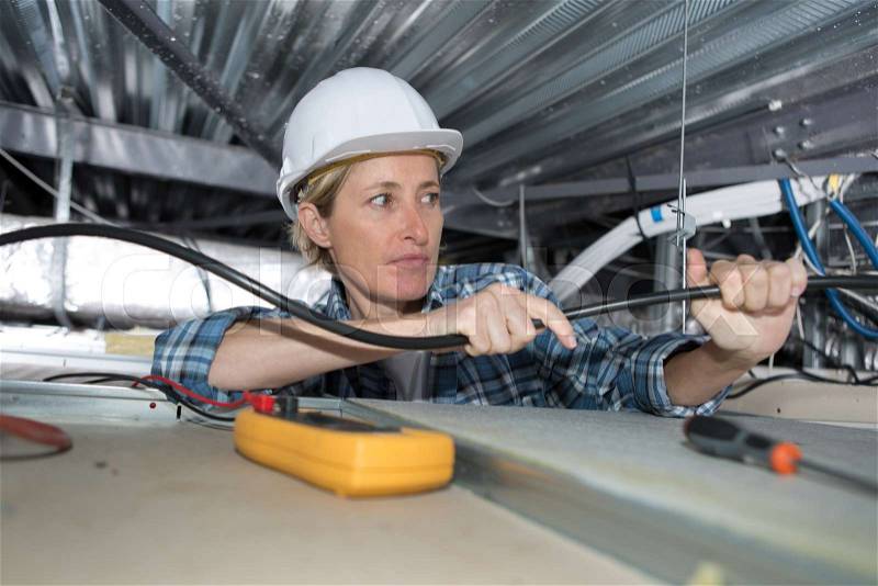 Female electrician installing ventilation in ceiling, stock photo
