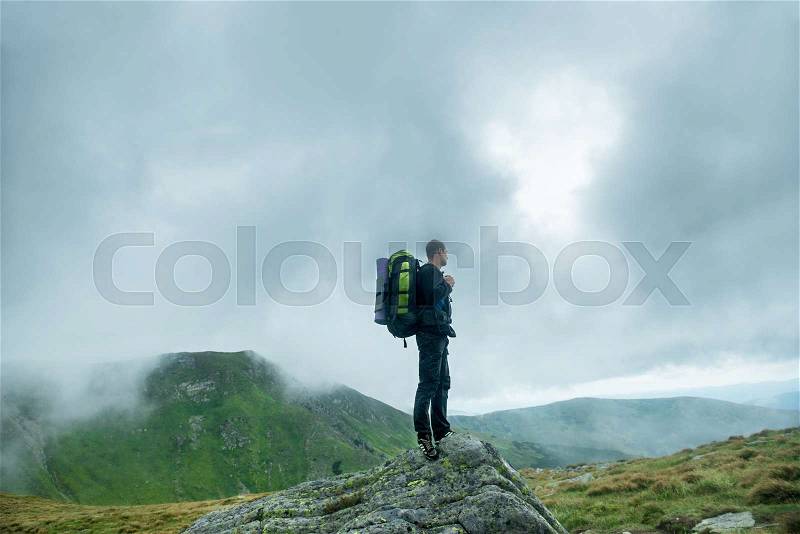 Traveler with backpack on the top of the mountain in the clouds, stock photo