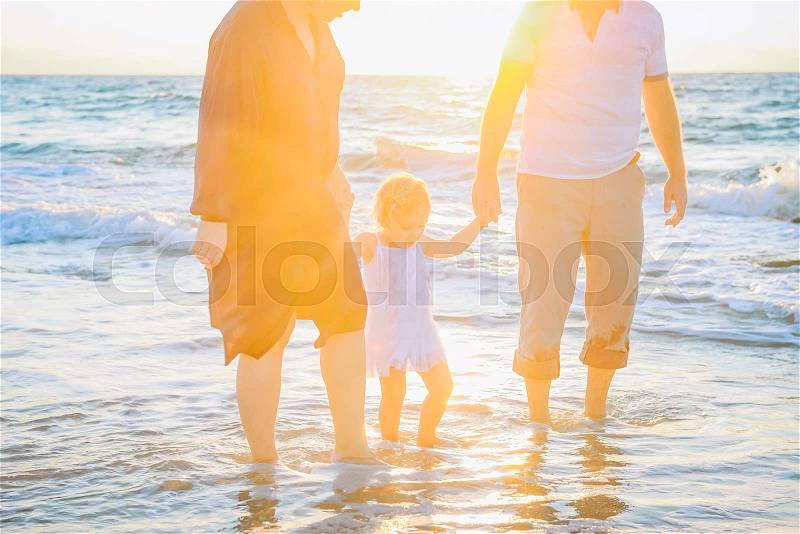 Close up Happy family of three - pregnant wife, father and daughter having fun walking on beach at sunset. Family traveling concept. Backlight, soft selective focus. Copy space, stock photo