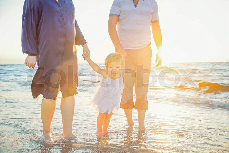 Close up Happy family of three - pregnant wife, father and daughter having fun walking on beach at sunset. Family traveling concept. Backlight, soft selective focus. Copy space, stock photo