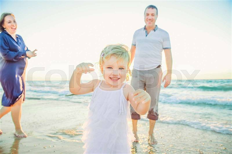 Laughing Baby girl running forward with smiling parents on the background. Happiness and harmony in family life. Happy family concept. Backlight, soft selective focus. Copy space, stock photo