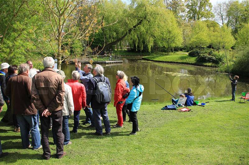 The guide is telling about the tree to the interesting people and the father is fishing with his sons in the pond in the park of the village Abbenbroek in beautiful spring, stock photo