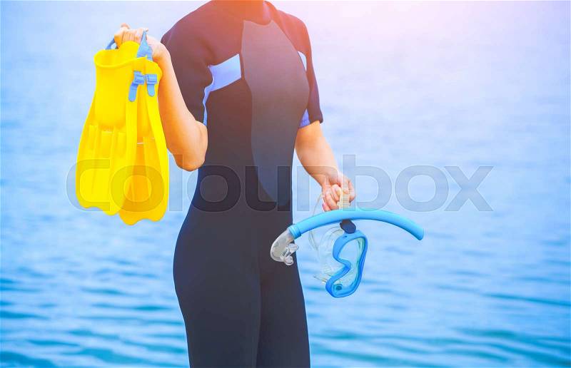 A girl diver in a wet suit holds a mask with a blue tube in her hands and a yellow fin in the other hand, stock photo