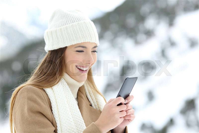 Happy lady using a smart phone in winter holidays in a snowy mountain, stock photo