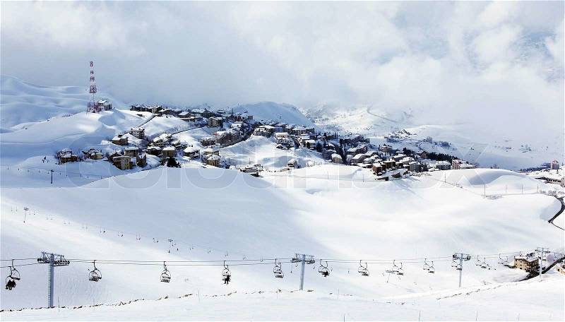 Winter mountain ski resort landscape with snow and cute little houses, chairlift with people playing sport, stock photo