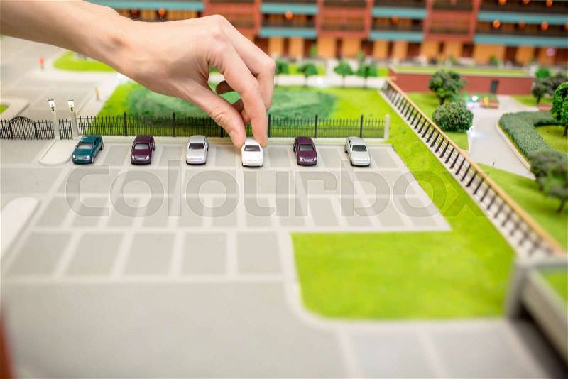Human hand taking one of car models from parking place on layout of modern city, stock photo