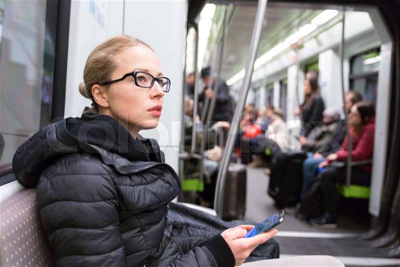 Young girl holding mobile phone while traveling on metro. Wireless internet on public transport concept, stock photo