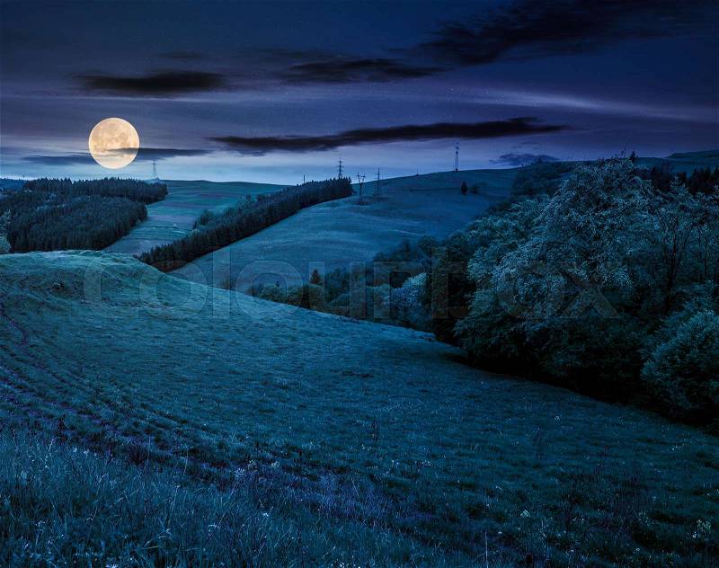 Lovely countryside with grassy hills at night in full moon light. beautiful nature of Carpathian mountains in springtime, stock photo