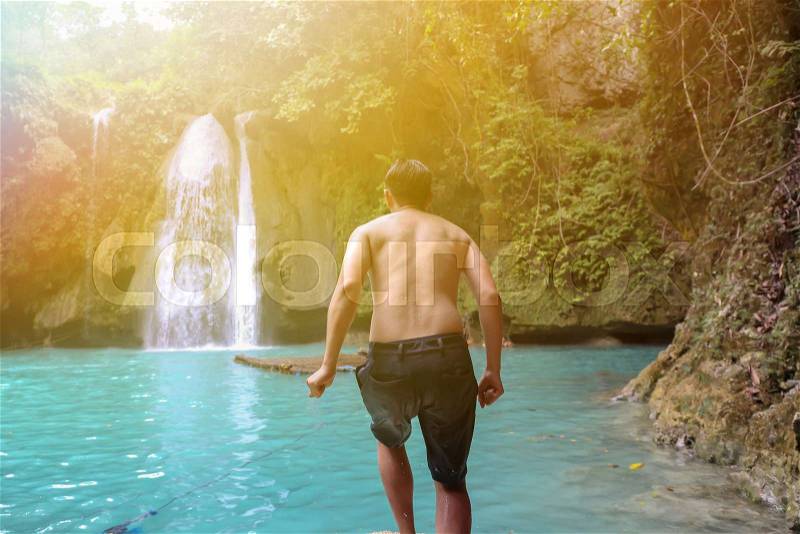 Young man moving forward to jump off the pond in waterfall scenery background, stock photo
