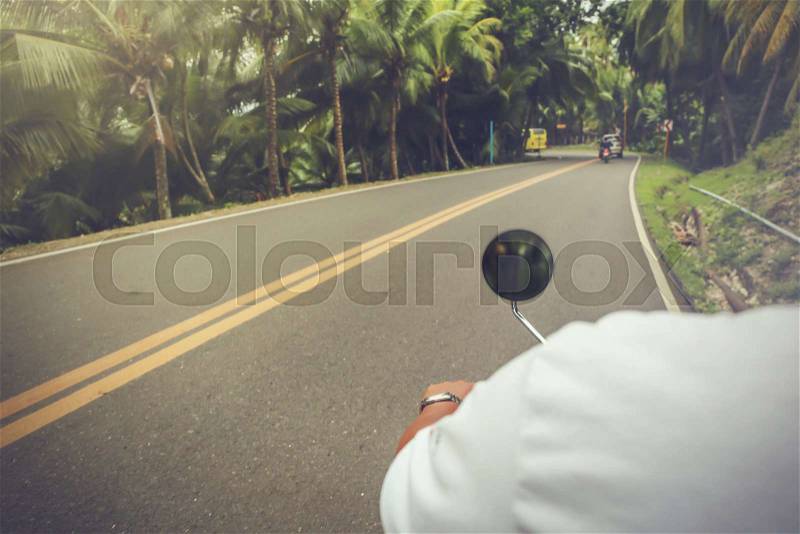 Close-up of motorcyclist riding motorbike transporting on road surrounded by summer jungle, stock photo