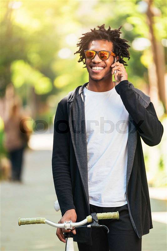 Afro young man using mobile phone and fixed gear bicycle in the street, stock photo