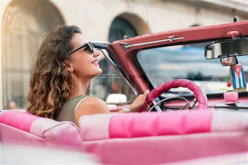 Beautiful woman tourist enjoying vacation holidays in Cuba driving a classic car, stock photo