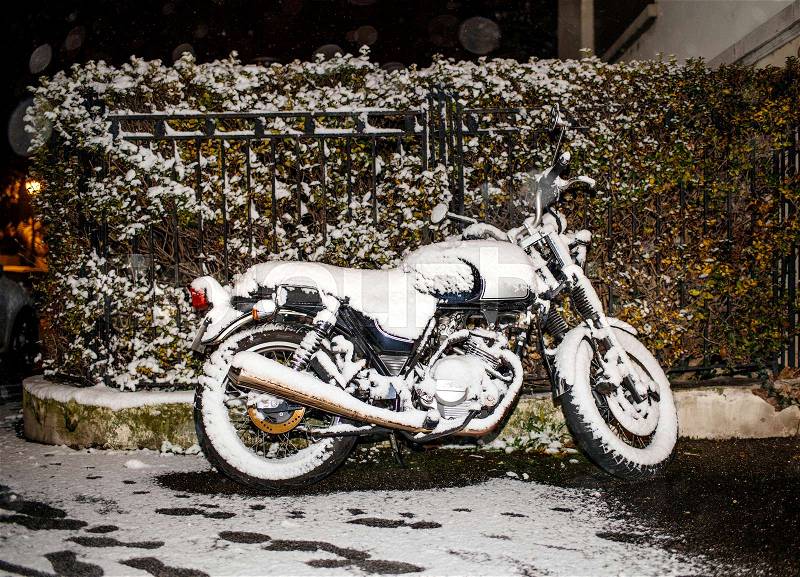 Motorcycle covered with snow at night parked near the fence of a house , stock photo