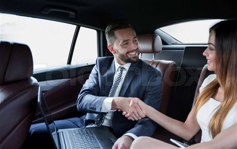 Businessman and businesswoman shaking hands after effective negotiations in the back seat of a car, stock photo
