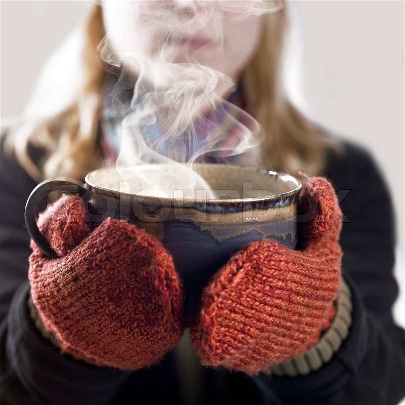 Detail of a woman with woolen gloves holding a hot steaming cup, stock photo