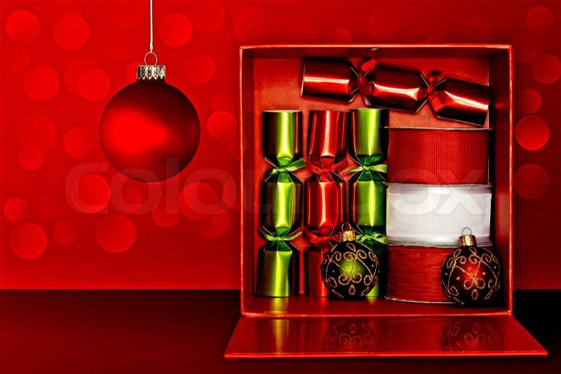 Red Gift Box Filled With Red & Green Party Favors, Decorative Red & White Ribbon And Red, Green & Gold Glitter Christmas Ornaments Over Red Textured Background With LED Lights, stock photo