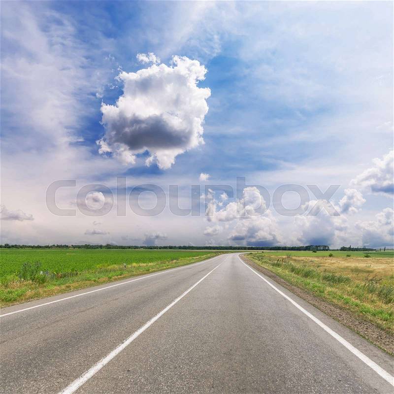 Asphalt road to horizon in field under low dramatic clouds, stock photo