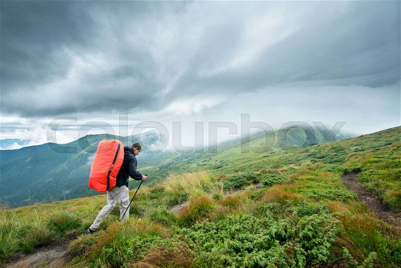 Traveler with trekking sticks and a backpack walks of the mountains in the clouds, stock photo