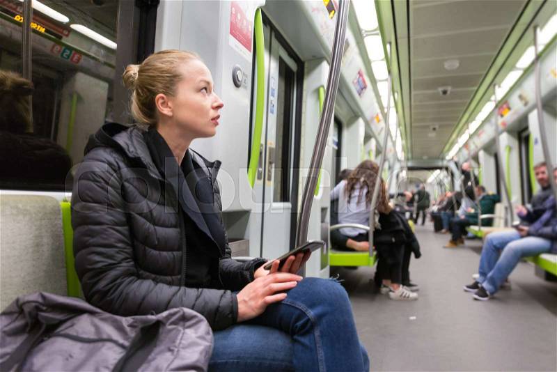 Young girl holding mobile phone while traveling on metro. Wireless internet on public transport concept, stock photo