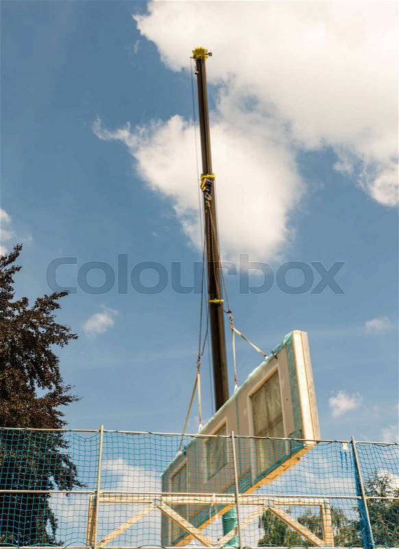 Assembling a prefabricated house - wall is hanging on a crane, stock photo
