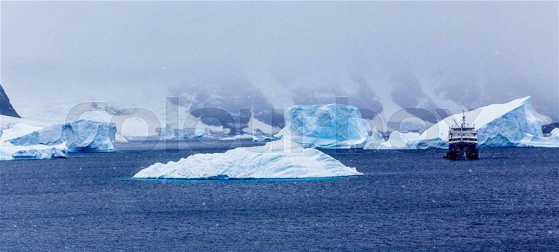 Snowfall and cruise ship among blue icebergs in Port Charcot, Booth Island, Antarctic, stock photo