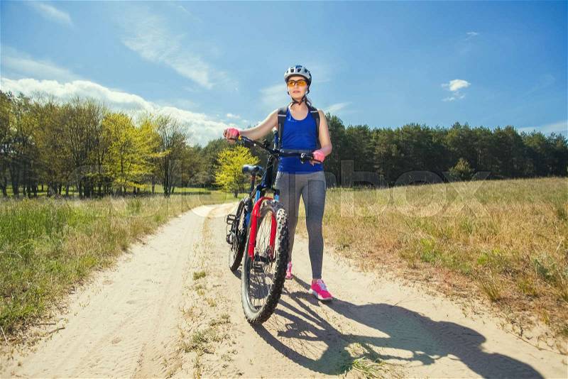 One young woman rides on a mountain bike outside of town on the road in the forest on a summer day, stock photo