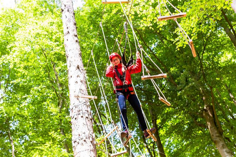 Child reaching platform climbing in high rope course in forest, stock photo