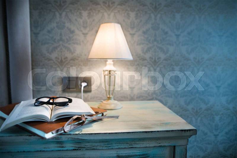 A lamp, a book and glasses on a bedside table in a hotel room, stock photo