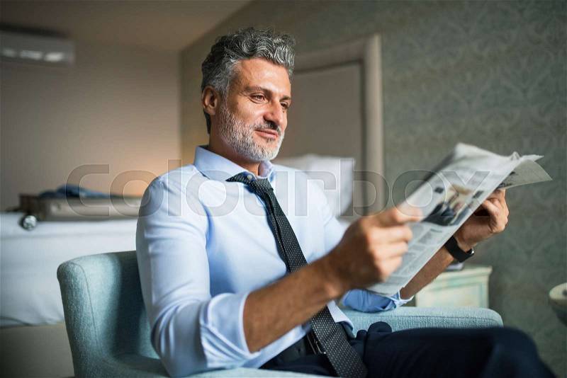 Mature, handsome businessman reading newspapers in a hotel room, stock photo