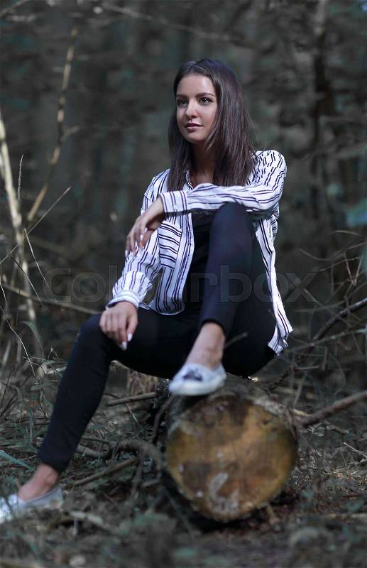 Portrait of beautiful young woman sitting on a log in the woods, stock photo