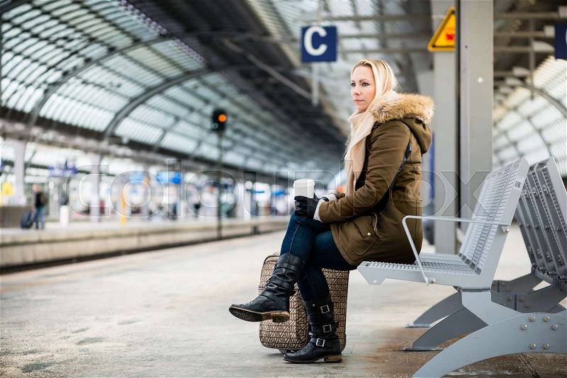 Woman on train station platform waiting on bench, stock photo