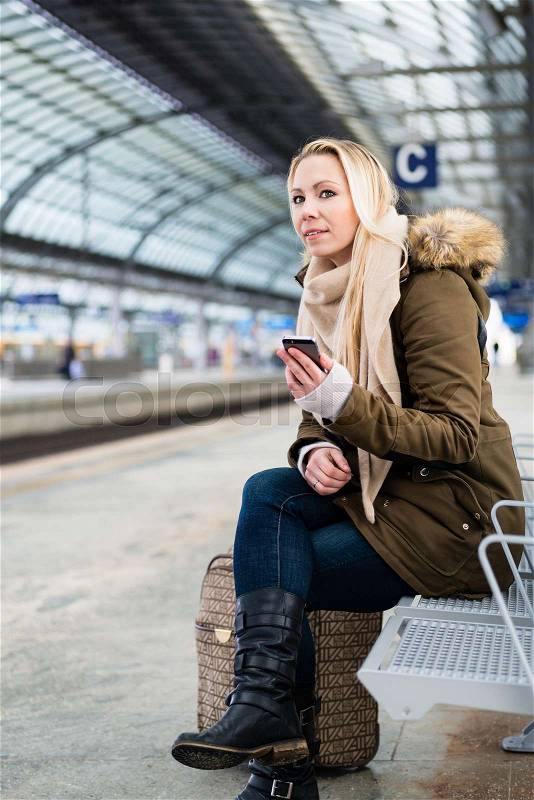 Woman on train station platform waiting on bench, stock photo