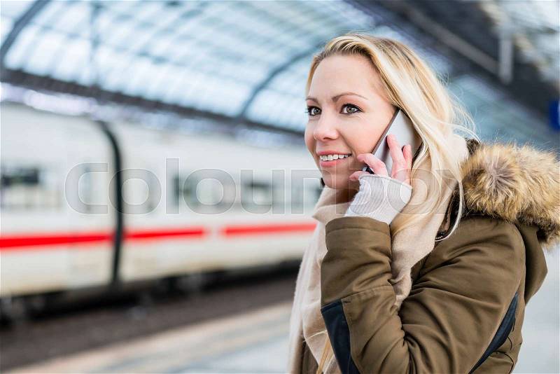 Woman using her telephone while modern train arrives in station, stock photo