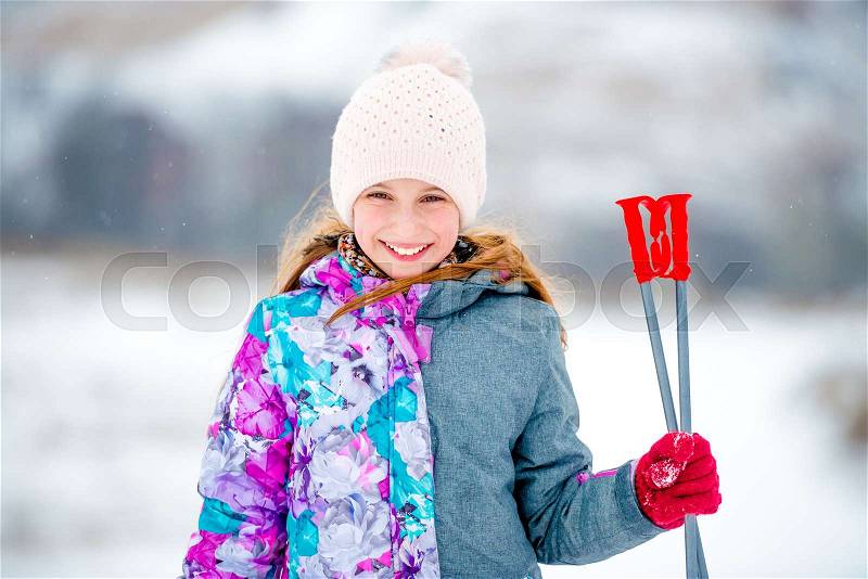 Adorable little girl holding ski sticks in hand and looking at camera, stock photo