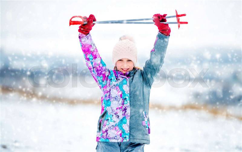 Active little girl in grey ski outfit holding ski poles in hands above her head, stock photo
