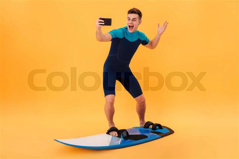 Full length photo of cheerful man surfing while taking selfie on mobile phone, isolated over yellow background, stock photo