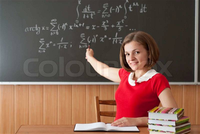 Young teacher is pointing on blackboard with math formulas, stock photo