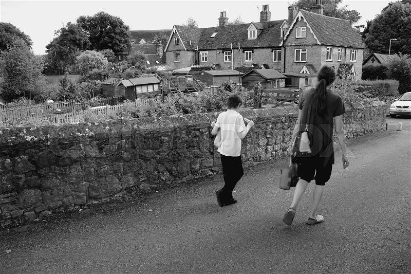 The mother is smoking a cigarette and her son is eating an ice cream and they walking over the mediaeval bridge in the village Aylesford in England in the summer in black and white, stock photo