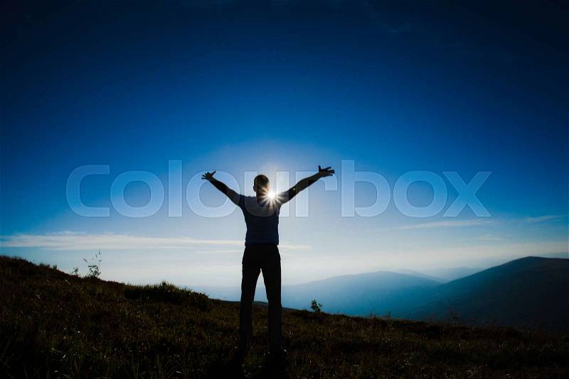 Silhouette of a person with hands up raised during the sunset on the top of the mountain, stock photo
