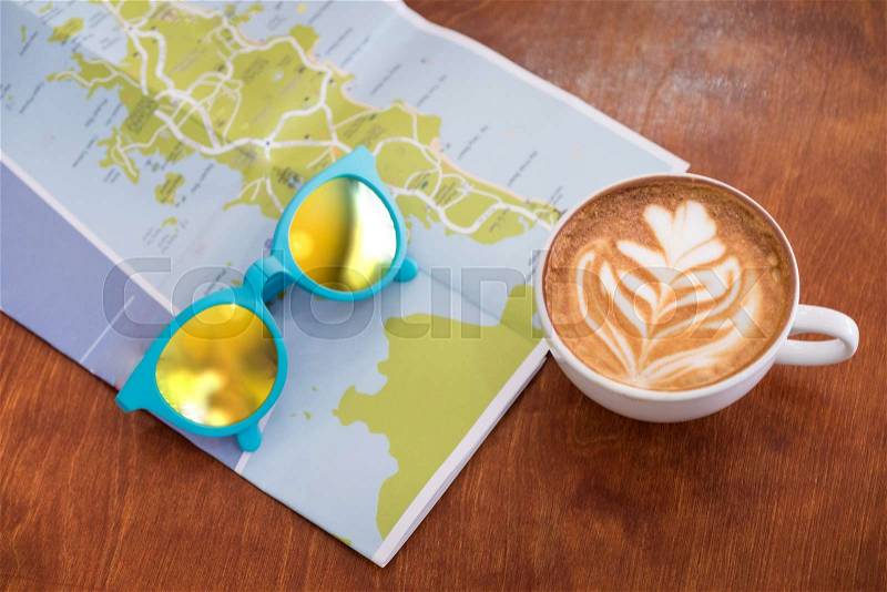 White coffee cup with latte art with travel map and sunglasses on brown wood table,Leisure activity, stock photo