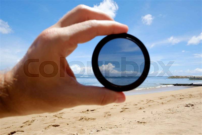 Polarizing filter hold against the beach giving clarity. Optics tool for lens in photography, stock photo