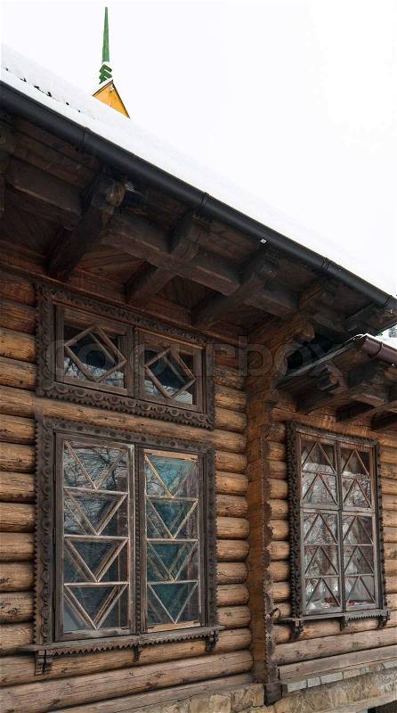 Fragment of country wooden house with snow on roof and carving window, stock photo