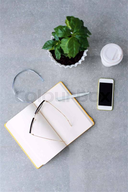 Office desk table with notebook planner, smart phone, glasses, coffee tree and coffee cup. Top view with copy space, stock photo