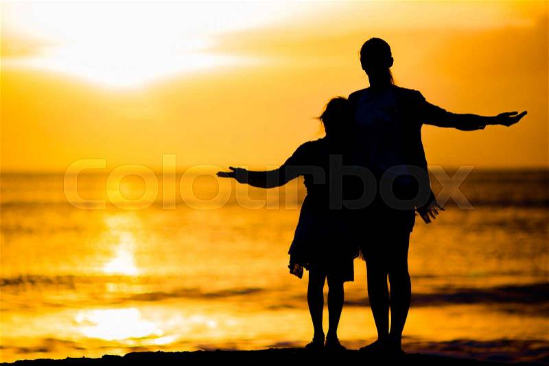 Little girl and happy mother silhouette in the sunset at the beach, stock photo