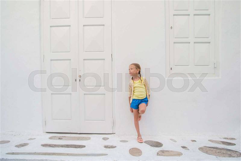 Little girl portrait outdoors in old greek village. Kid at street of greek village with white walls and colorful doors, stock photo